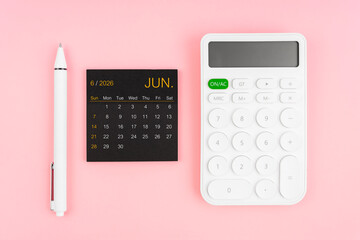 June 2026 calendar and white calculator with pen on pink color background.