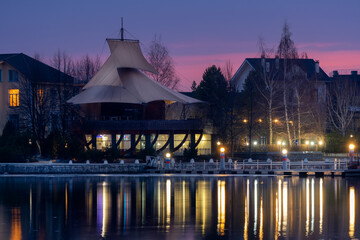 The yacht club building decorated with sails on the shore of a reservoir on a spring night