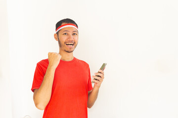 Young Indonesian man with fist clenched holding  mobile phone with headband in isolated white