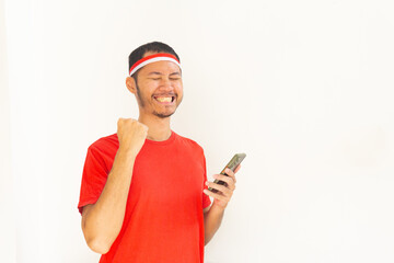 Young Indonesian man with fist clenched holding  mobile phone with headband in isolated white