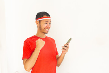 Young Indonesian man with fist clenched holding  mobile phone with headband in isolated white