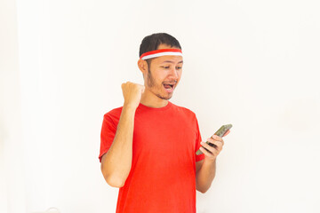 Young Indonesian man with fist clenched holding  mobile phone with headband in isolated white