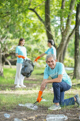 portrait asian senior man picking up used plastic bottle on ground with background diverse team of...