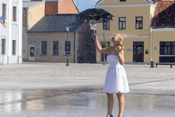 A woman in a white dress with a black umbrella dancing in the rain