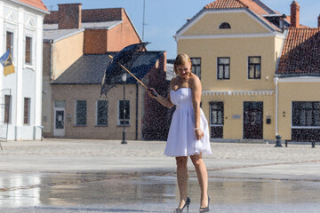 A woman in a white dress with a black umbrella dancing in the rain