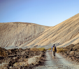 A man is traveling, hiking among mountains and volcanoes in the desert with a backpack.