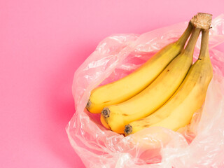 Bananas with spoiled skin in a plastic bag on a pink background