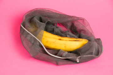 Banana with damaged skin in an eco-bag on a pink background. Save the lonely banana