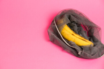 Banana with damaged skin in an eco-bag on a pink background. Save the lonely banana