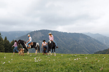 A group of people and horses are in a field of flowers. Two ride horses while two others walk.
