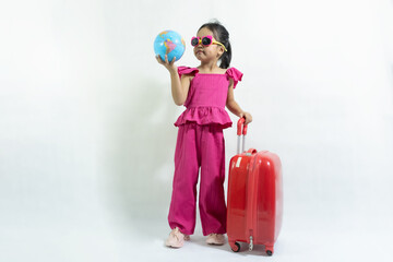 Baby girl holding the world map, wear casual clothes  in pink dress and shoes posing next to red suitcase. Tourist travel abroad in free time rest. Traveler and flight trip concept.