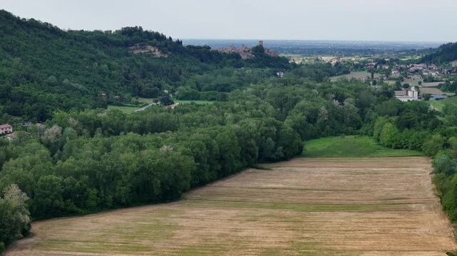 Slow motion aerial panorama revealing verdant countryside and historic Canossa Castle nestled among rolling green fields in Emilia Romagna, Italy