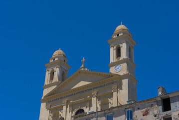 Fototapeta premium A grand, ornate church with two prominent bell towers and a clock on one, stands under a clear blue sky, with other buildings and a mountain visible in the background.