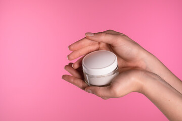 Hand Holding White Cream Jar on Pink Background