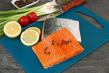 Fresh salmon with lemon, spring onions and tomatoes on a cutting board.