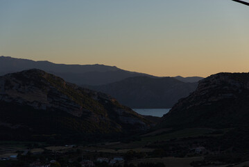 The bright sun sets behind a silhouetted mountain range, casting a warm orange and yellow glow across the sky with soft blue at the top.