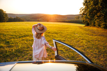 Travel by car on summer vacation. Carefree woman enjoying sunset during road trip in idyllic...