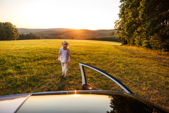 Woman walking away from car into summer sunset field. Concept of freedom, escapism and joy of travel