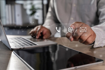 Contact us Business professional using digital icons for communication tablet with laptop background, showing modern technology and connectivity