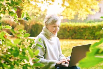 Outdoor portrait of mature 55 - 60 year old woman using laptop in garden
