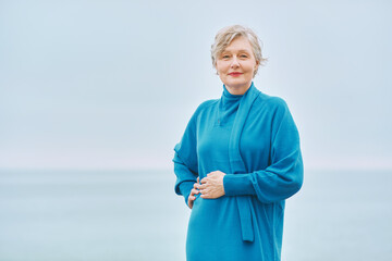 Fashion portrait of beautiful mature woman wearing blue cyan dress posing outdoors