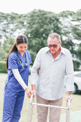 Home caregiver assists elderly man with walker outdoors, providing support and encouragement in...