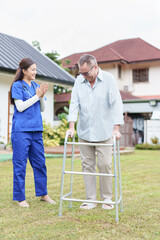 Elderly man using walker outdoors with supportive female nurse, rehabilitation, recovery, and...