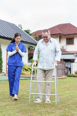 Home caregiver supports elderly man using walker outdoors, showing encouragement and care in...