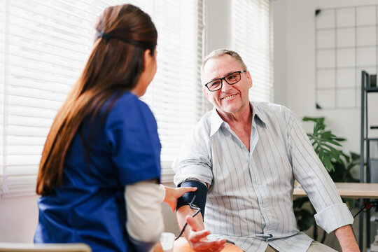 Home caregiver checking blood pressure of elderly man in bright living room, showing care and support with warm smile, health monitoring and comfort at home