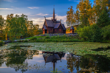 Historic Garmo Stave Church in Lillehammer, Norway, also known as Garmo stavkirke, reflected in a lily-covered pond at sunset.