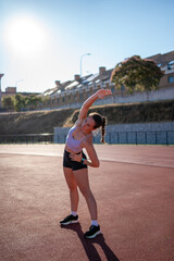 Young athlete stretching on running track in sunlight