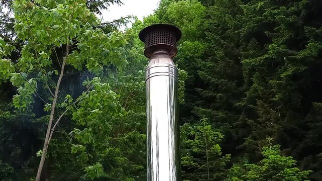 Thick smoke rises steadily from a vertical metal chimney pipe in an outdoor setting. The scene conveys warmth, combustion, or industrial activity. Perfect for themes like heating, energy