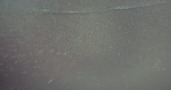 close up of a line of foam washes over the rain soaked sand.