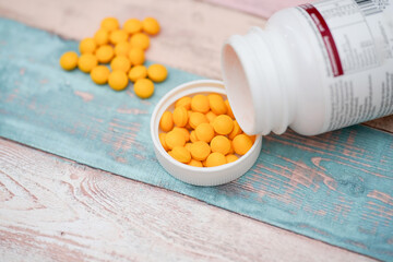 Container of yellow tablets spilled on wooden surface with more tablets in background