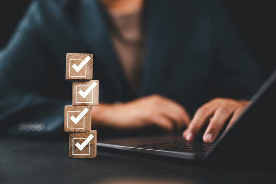 Businessman planning checklist using wooden cubes with check marks, productivity goal setting and time management strategy concept for corporate success and effective work organization.