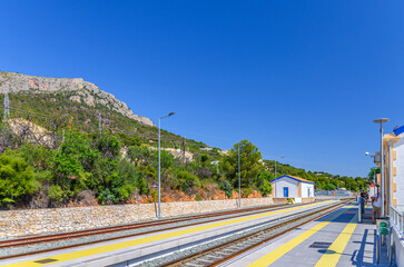 Tram rails in railway station small train station of Calpe town and Sierra de Olta mountain range background in sunny summer day, Alicante province, Valencian Community, Spain