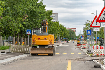 Large construction site on a road with a yellow excavator and barriers. Traffic signs, residential...