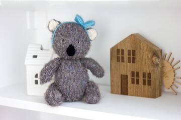 Gray knitted amigurumi bear toy on a white shelf in the interior of a children's room