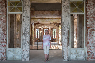 Mature adult woman stands in the doorway of a hall of an abandoned ancient castle or palace.