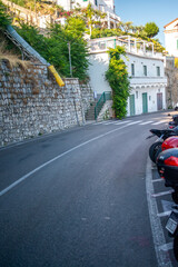 A picturesque street scene from the Amalfi Coast, featuring narrow cobblestone pathways, colorful Mediterranean buildings, flower-laden balconies, and local life