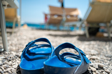 A close-up photo of a pair of summer slippers gently resting on golden beach sand, with soft sea...