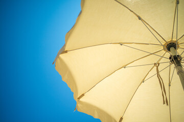 A vibrant beach umbrella seen from below, with clear blue sky and golden sunlight in the background.