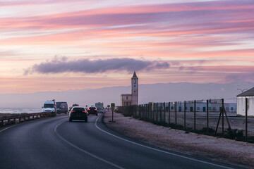 Distant View of Las Salinas Church at Sunset with Coastal Road and Pink Sky. Cabo de Gata Landscape, Almería