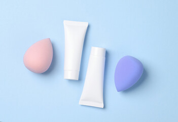Make-up puffs for foundation and tubes of cream on a blue background. Beauty concept