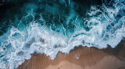 Aerial view of ocean waves crashing on a sandy beach, showcasing a dramatic contrast between the deep blue water and the white foam, meeting a tan shoreline