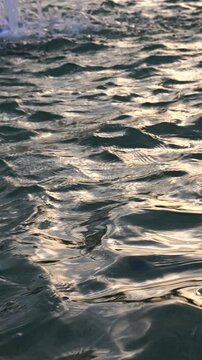 Abstract water surface background: vertical mobile video of water waves during sunset