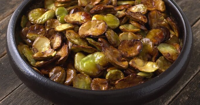 Homemade roasted broad beans (Vicia faba) in a bowl. Selective focus, table spin.