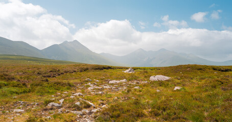 A grassy landscape with some rocks in the near distance and mountains in the far distance, under a cloudy sky. It is in Strickeen, which is in County Kerry, Ireland.