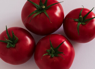 Close-up of four juicy red tomatoes with green stems on a white surface. Fresh organic vegetables...