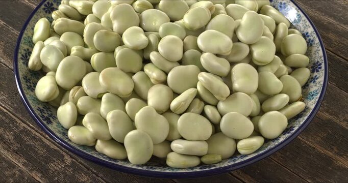 Raw fava beans (Vicia faba) with the second skin on a platter. Selective focus, table spin. 